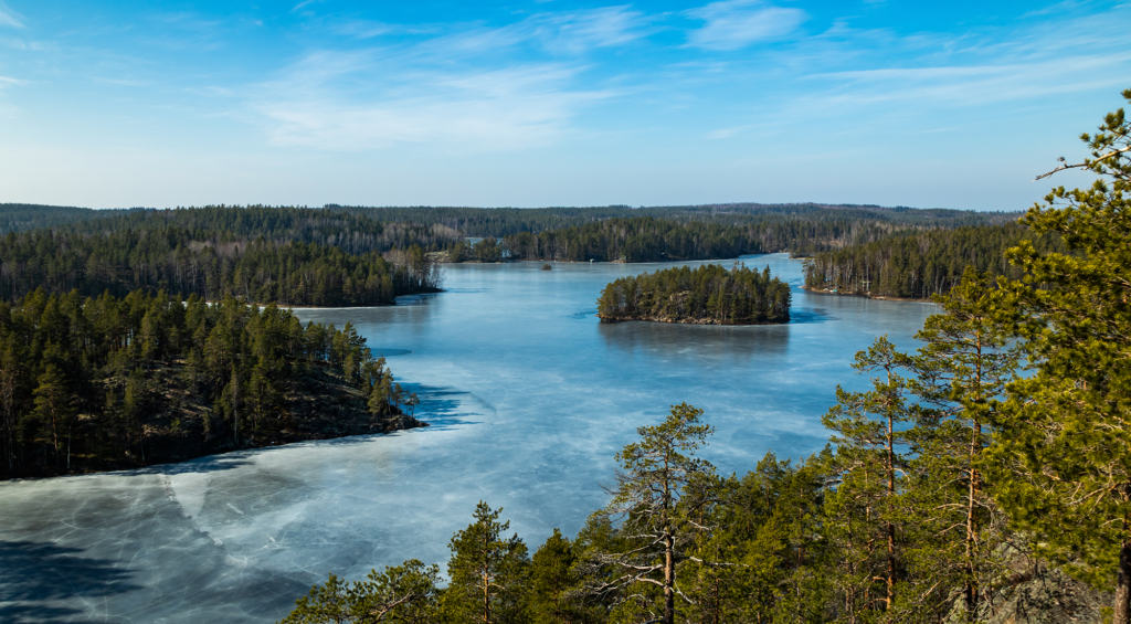Suur-Savon Sähkön brändikuva suomalaisesta luontomaisemasta. Maisemassa näkyy metsien keskellä järvi, jossa on saari. Sininen taivas heijastuu järven pinnasta.